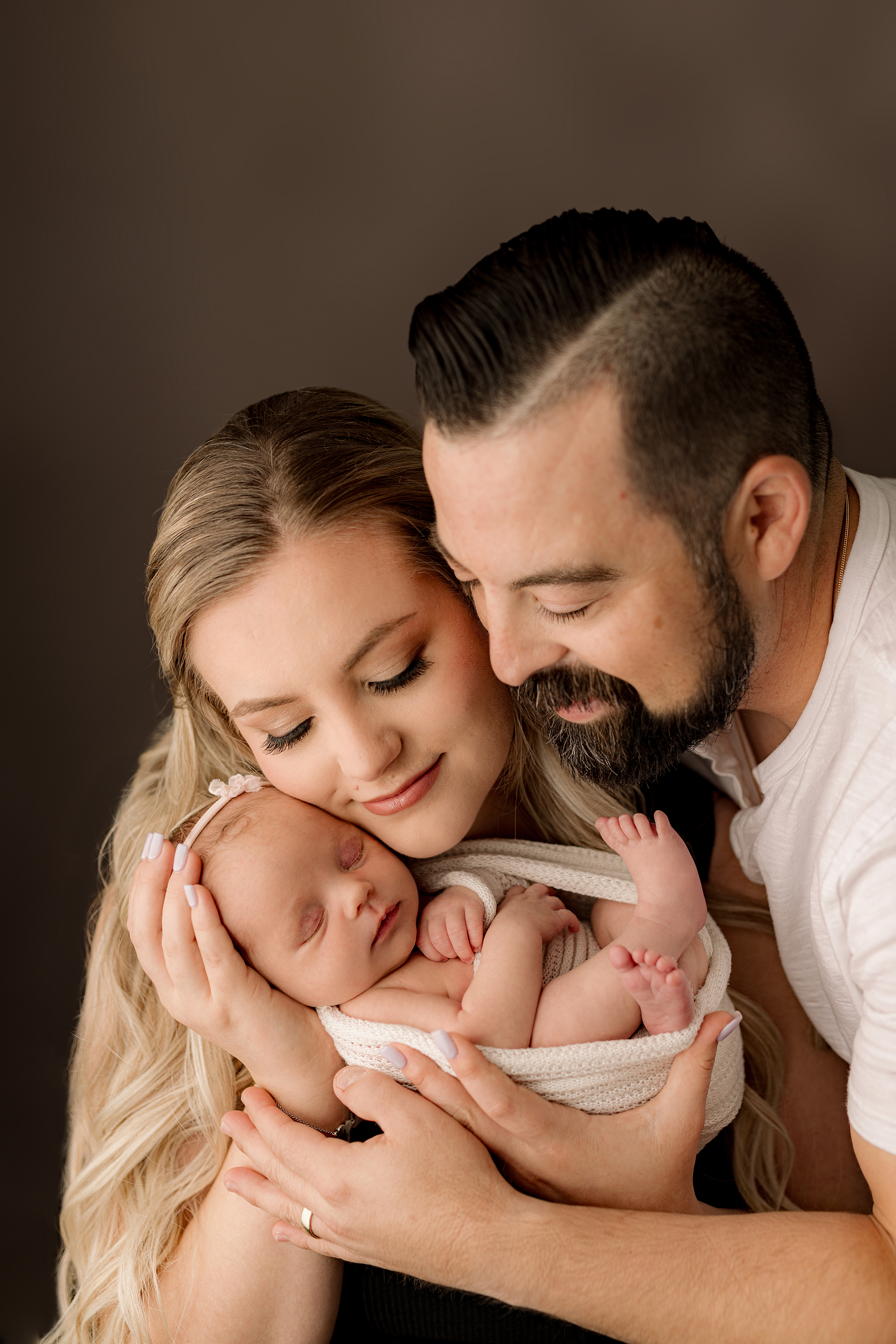 two young parents snuggle new baby daughter while closing their eyes