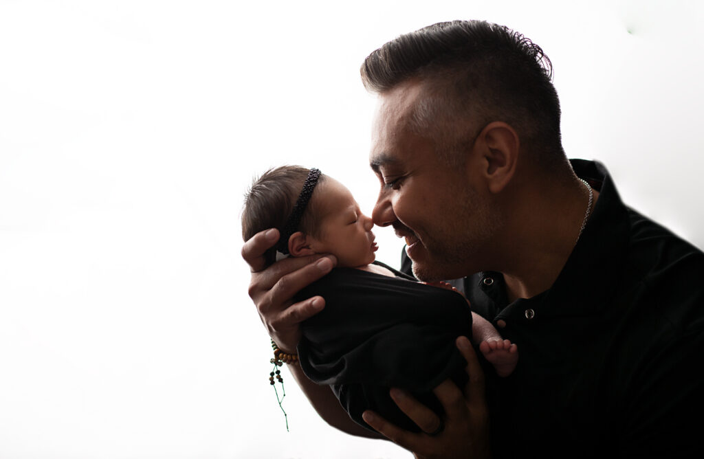 dad holds newborn daughter wrapped in black blanket 