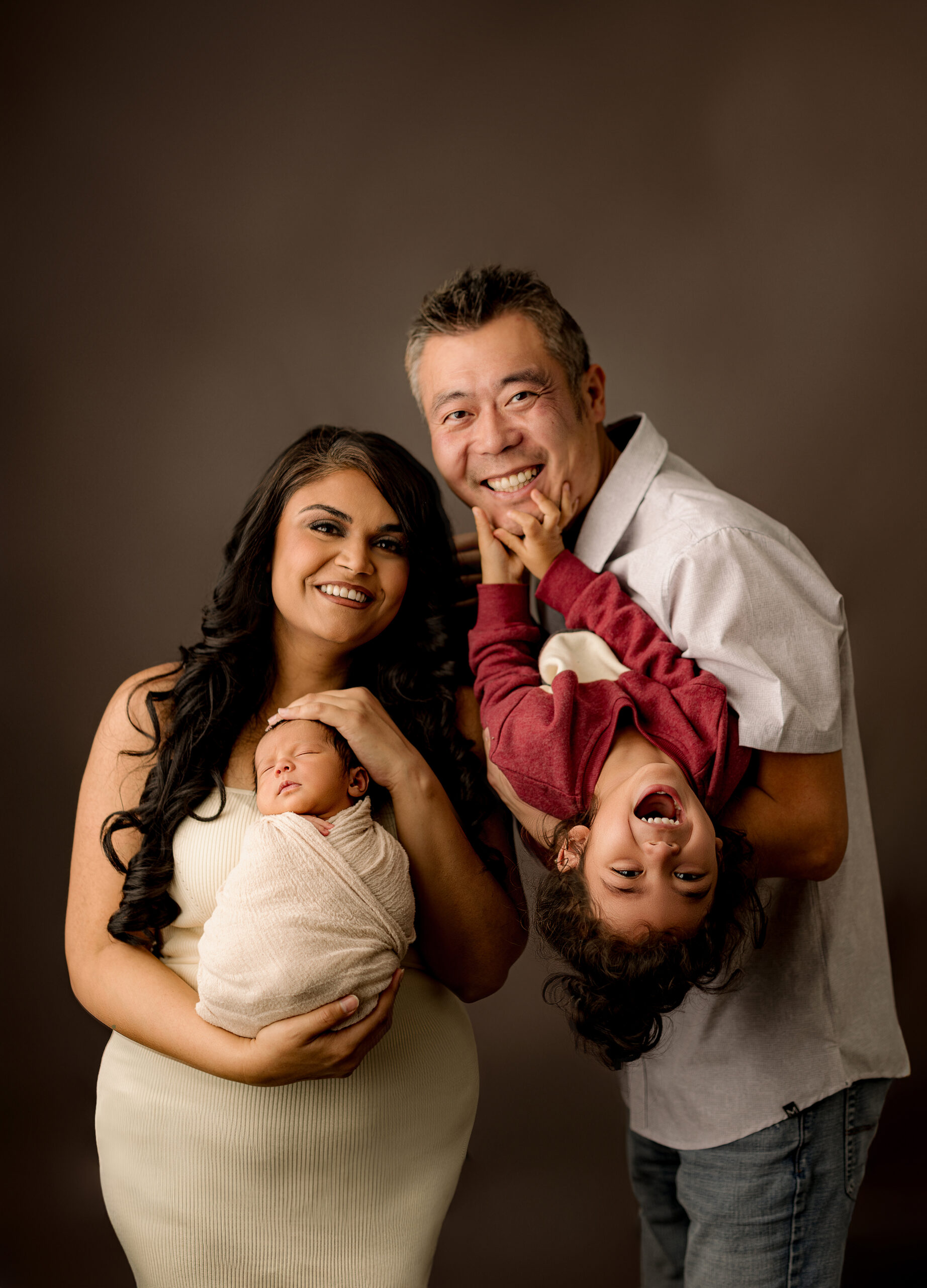 dad holds toddler upside down white mom holds newborn abby boy wrapped in white blanket