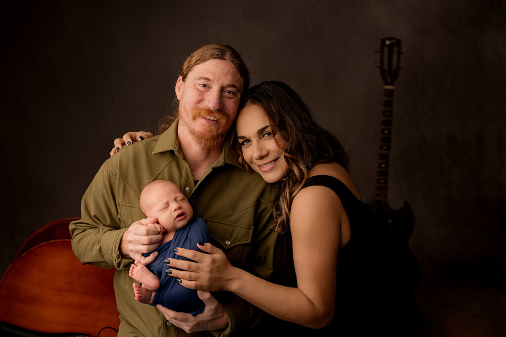 mom hugs dad while he holds newborn baby boy wrapped in blue blanket