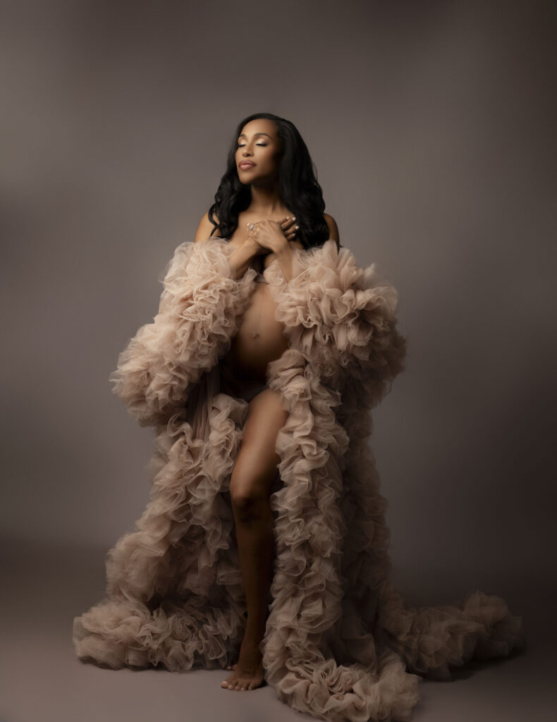 beautiful pregnant mother poses with hands overlapping on her chest in a pink tulle robe 