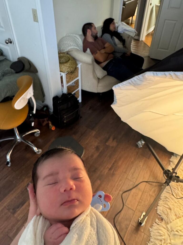 Photographer holds baby while parents sleep in the background at Austin newborn photography studio 