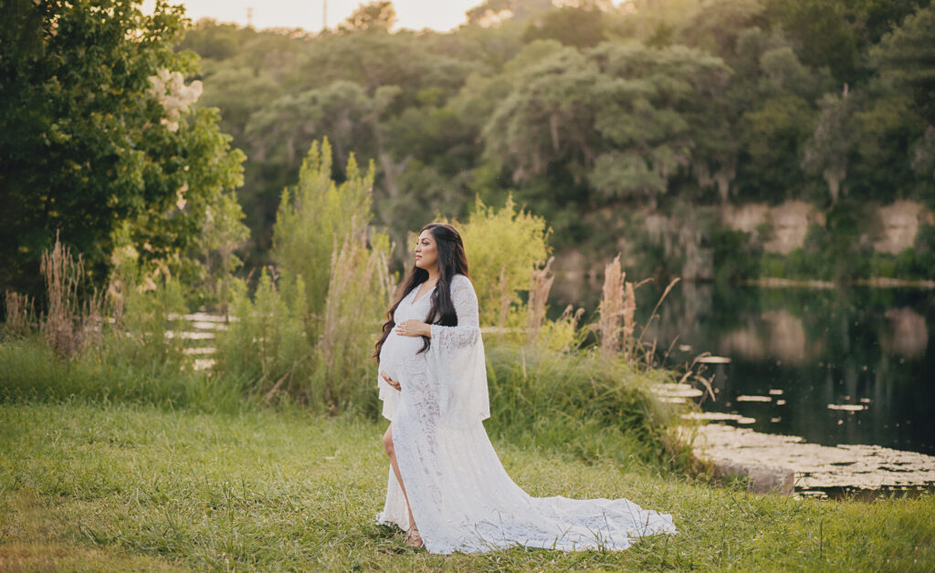Pregannt mother poses in white lace dress ar an outdoor maternity session In austin texas